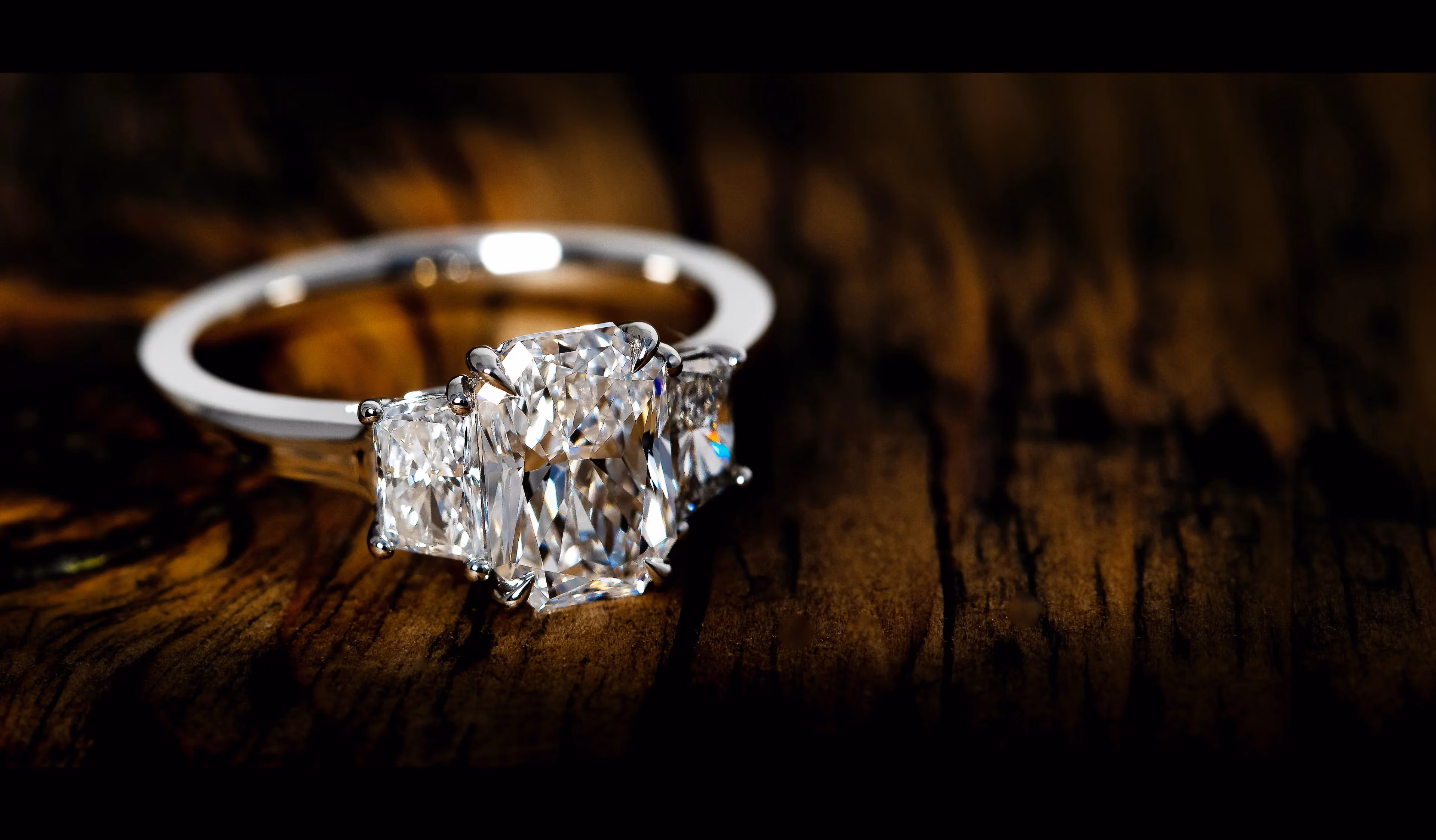A radiant-cut diamond ring with two diamond side stones on dark wood